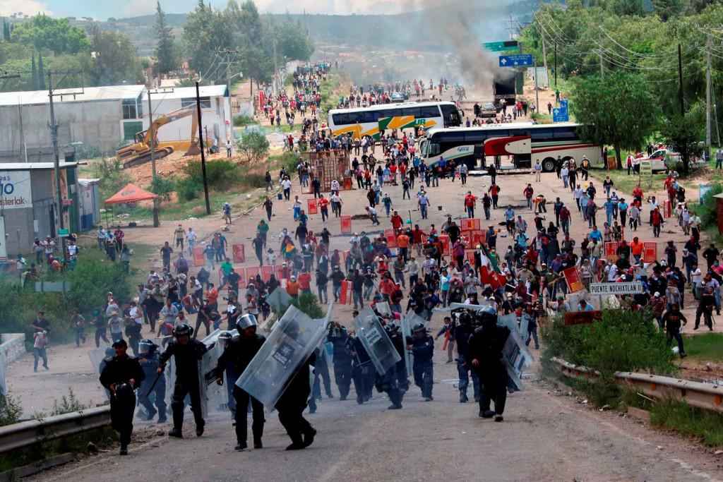 Riot police are forced to fall back as they battle with protesting teachers who were blocking a federal highway in the state of Oaxaca, near the town of Nochixtlan, Mexico, Sunday, June 19, 2016. The teachers are protesting against plans to overhaul the country's education system which include federally mandated teacher evaluations.(AP Photo/Luis Alberto Cruz Hernandez)