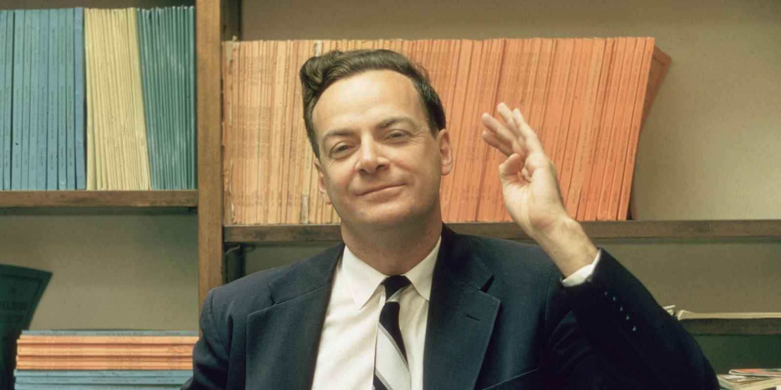 1959:  American physicist Richard Feynman (1918 - 1988) stands and raises one hand, in front of some shelves at Cal Tech University, Sacramento, California.  (Photo by Joe Munroe/Hulton Archive/Getty Images)